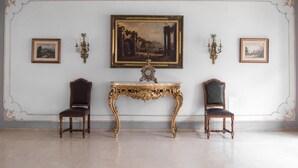 Une pièce comprenant un grand tableau encadré, deux chaises, une table et des appliques murales.