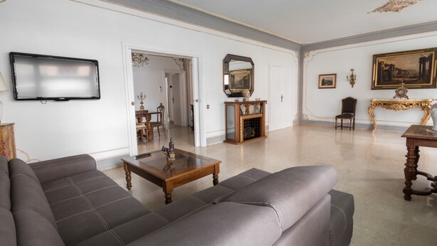 Un salon spacieux avec un canapé gris, une table basse en bois et un téléviseur fixé au mur.