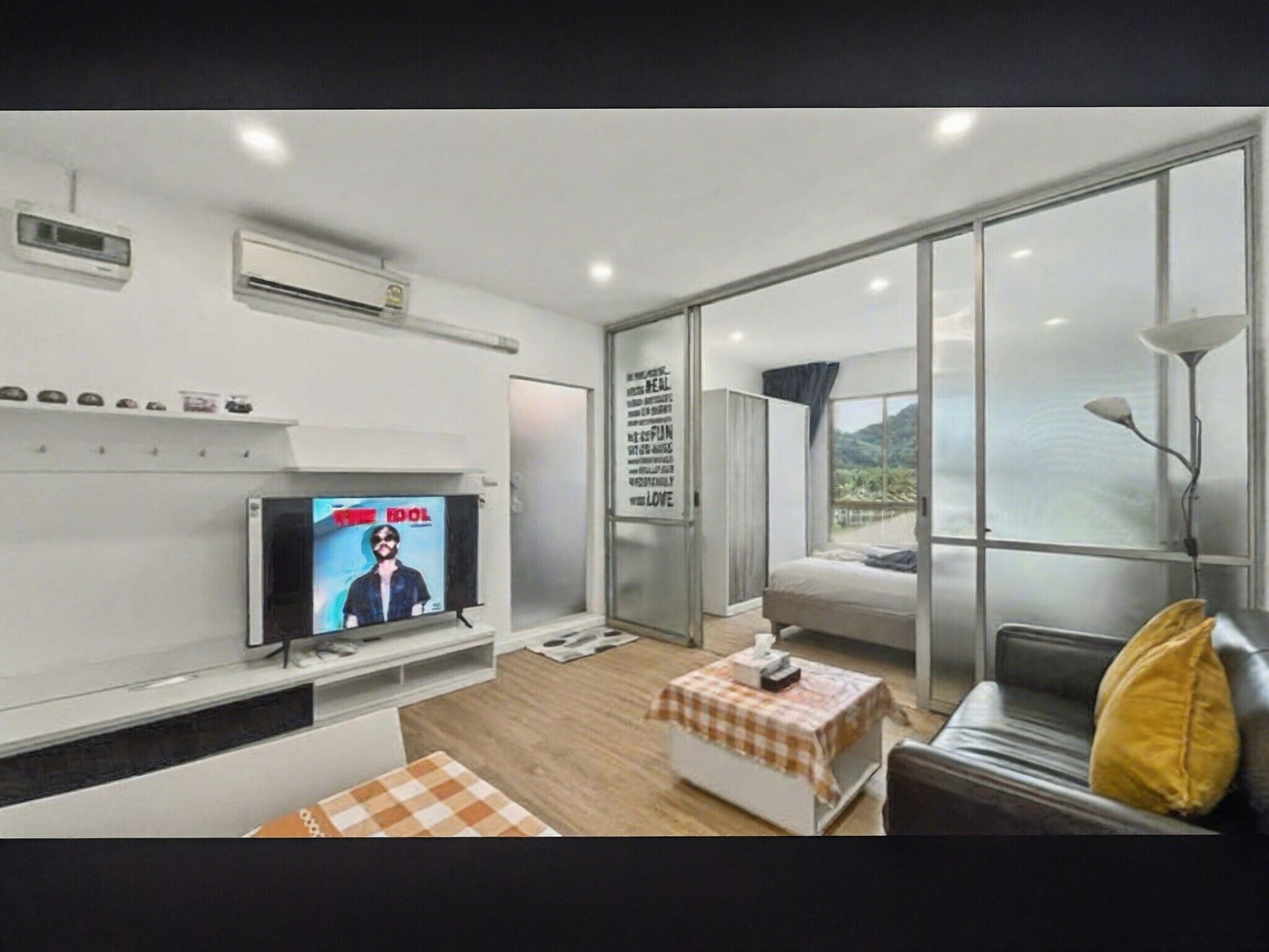 Una sala de estar moderna con un televisor de pantalla plana, un sofá, una mesa de centro y un ventanal con vistas al exterior.