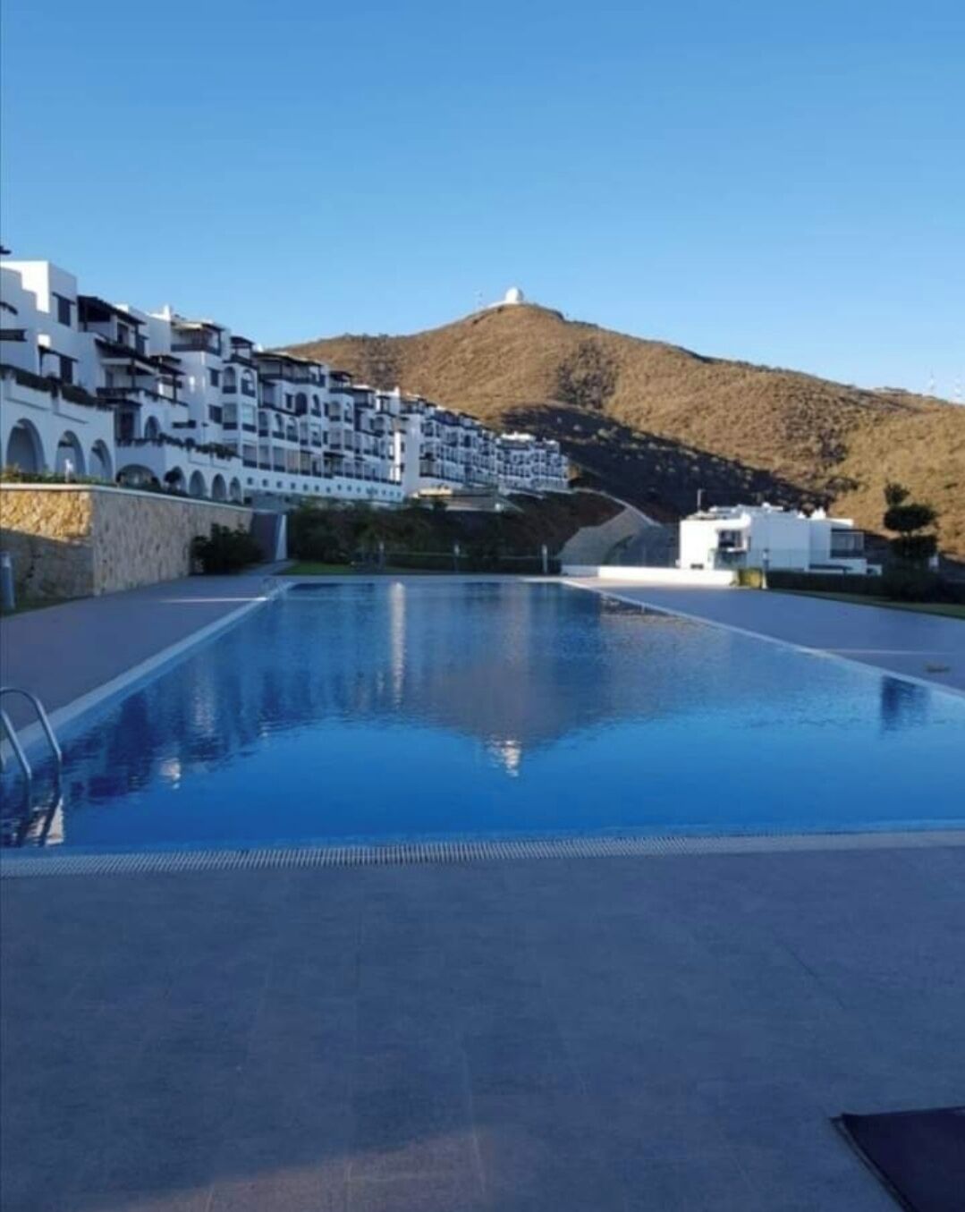 Una piscina con vista chiara su un pendio collinare e edifici moderni sullo sfondo.