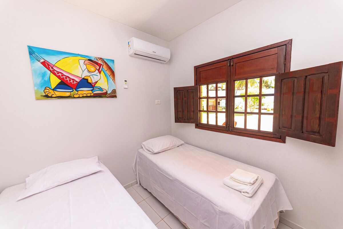 Una habitación con dos camas individuales, un cuadro en la pared, un equipo de aire acondicionado y una ventana con contraventanas de madera.