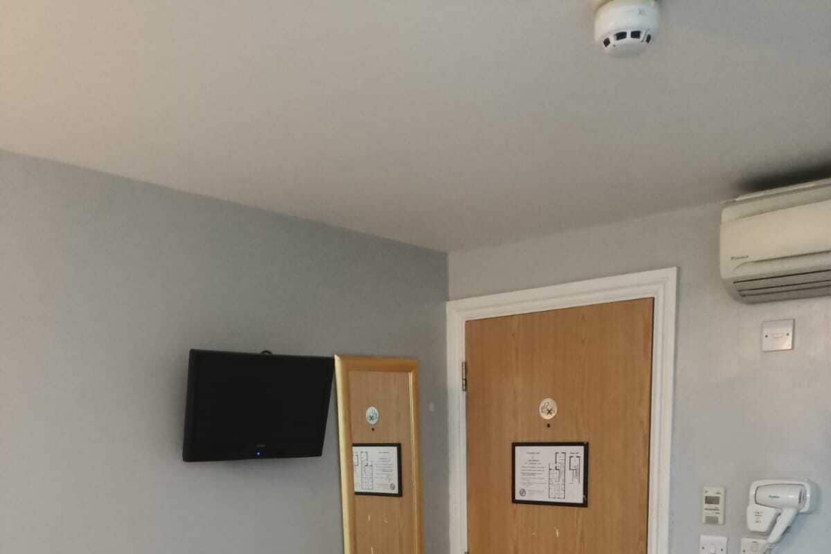 A hotel room with two single beds, a wooden door, a mounted television, a chair, and a telephone.