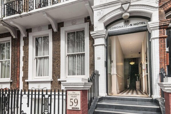 The Coronation Hotel at 59 Capilion, featuring a traditional facade with white and brick detailing, a prominent entrance, and a black metal fence. - Coronation Hotel (London)