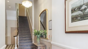 Un escalier avec un sol à carreaux, un lustre, un miroir et un tableau encadré au mur.