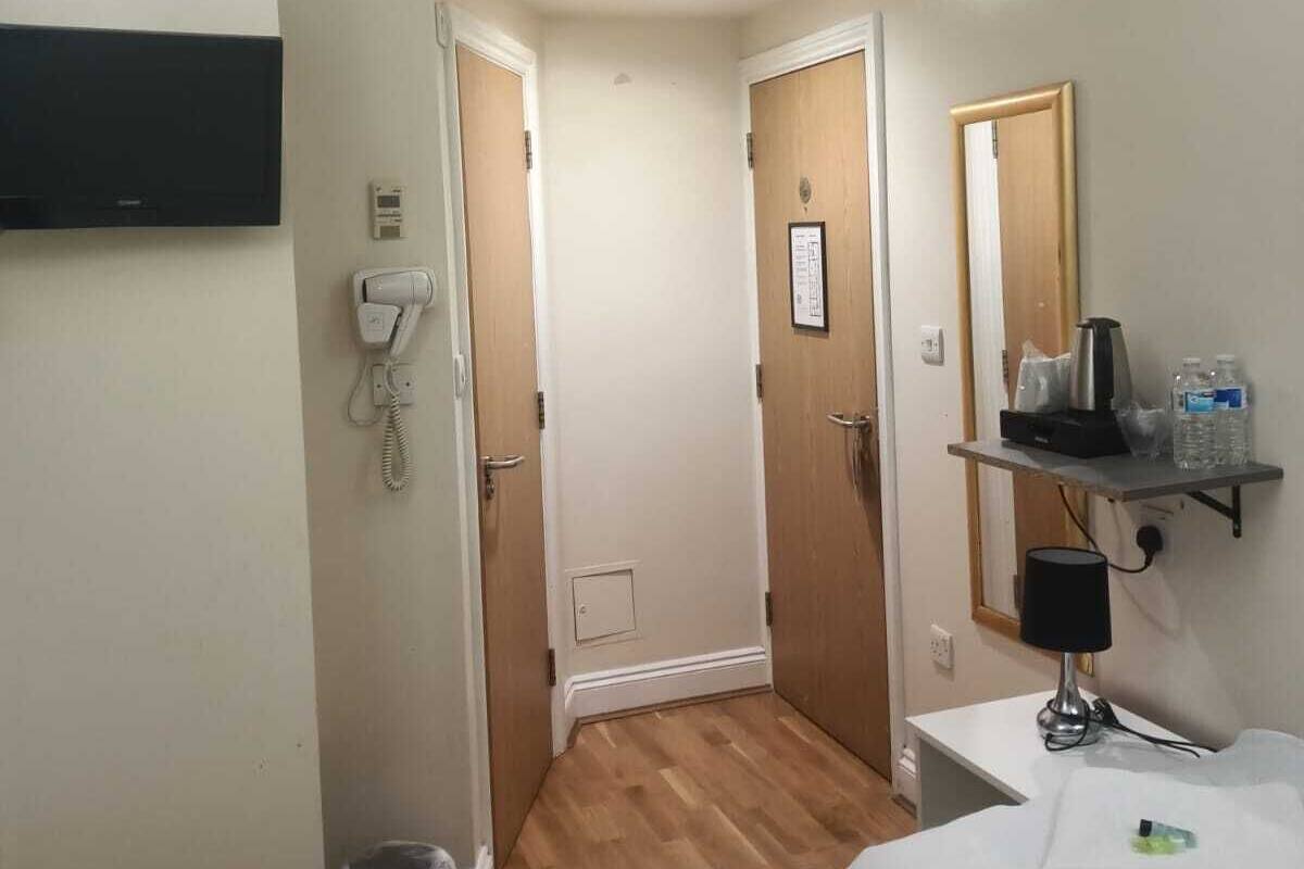 A hotel room with two beds, a mounted TV, a phone, a small trash bin, a shelf with toiletries, and a mirror.
