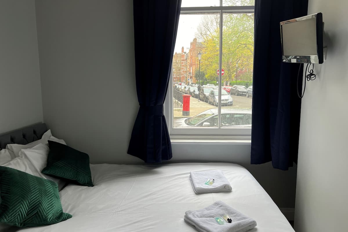 A hotel room with a bed, a window with curtains, a wall-mounted TV, and a view of parked cars outside.