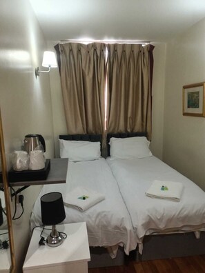 A hotel room with two beds, a bedside table with a lamp, a coffee maker, and a framed picture on the wall. - Coronation Hotel (London)