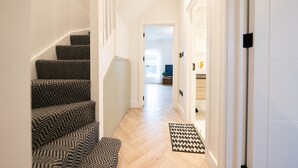 A staircase with patterned carpet leading to a room with a wooden floor and a black and white rug.