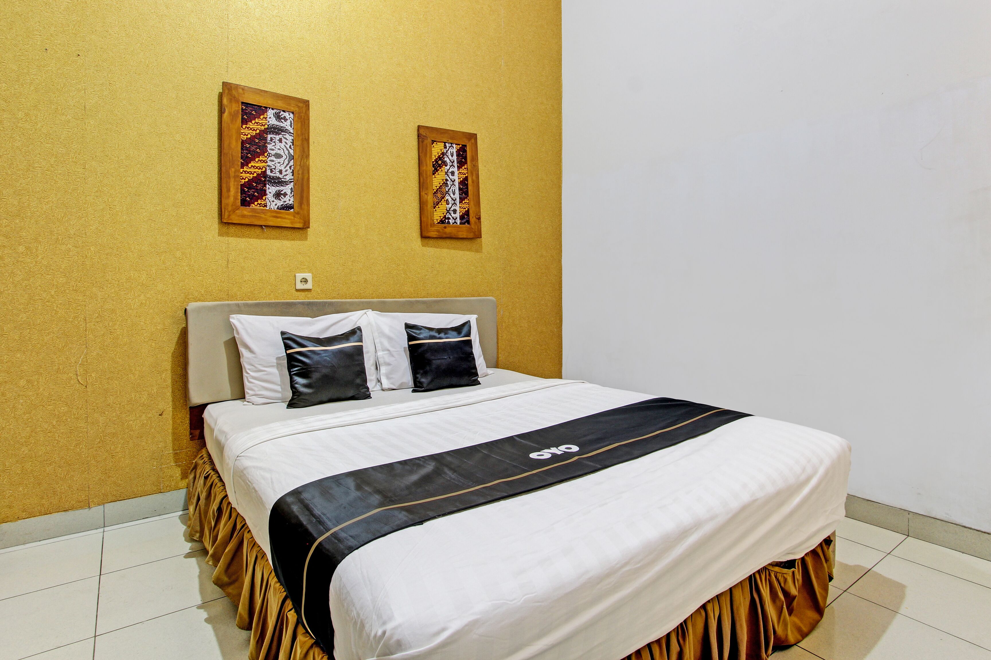 Habitación de hotel con cama, dos almohadas, colcha blanco y negro, y dos cuadros en la pared.