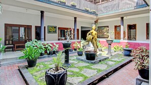 A courtyard with potted plants, a statue, and a traditional building with a balcony. - Super OYO Capital O 93240 Candra Dewi Hotel (Yogyakarta)