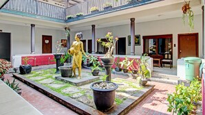 A courtyard with a statue, potted plants, and a wooden balcony. - Super OYO Capital O 93240 Candra Dewi Hotel (Yogyakarta)