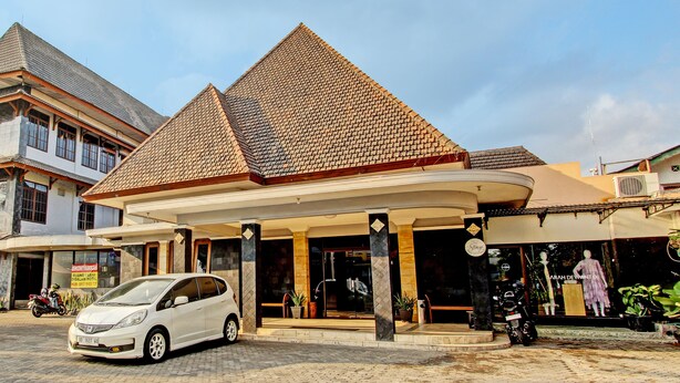 A hotel with a traditional architectural style, featuring a prominent pyramid-shaped roof and a covered entrance area with potted plants. - Super OYO Capital O 93240 Candra Dewi Hotel (Yogyakarta)