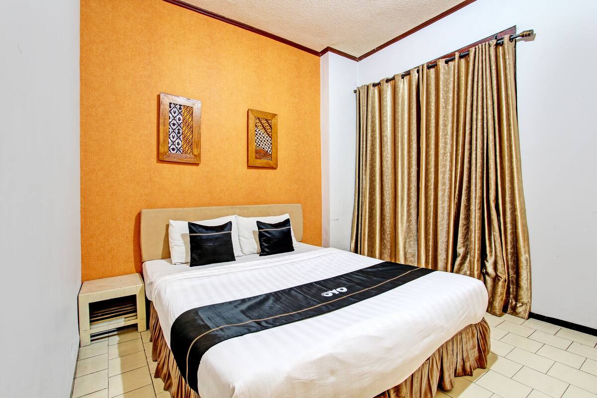 A hotel room with a bed, a nightstand, and two framed pictures on the wall.