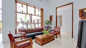 A spacious living room with a large window, a wooden coffee table, a sofa, and two armchairs. - Super OYO Capital O 93240 Candra Dewi Hotel (Yogyakarta)