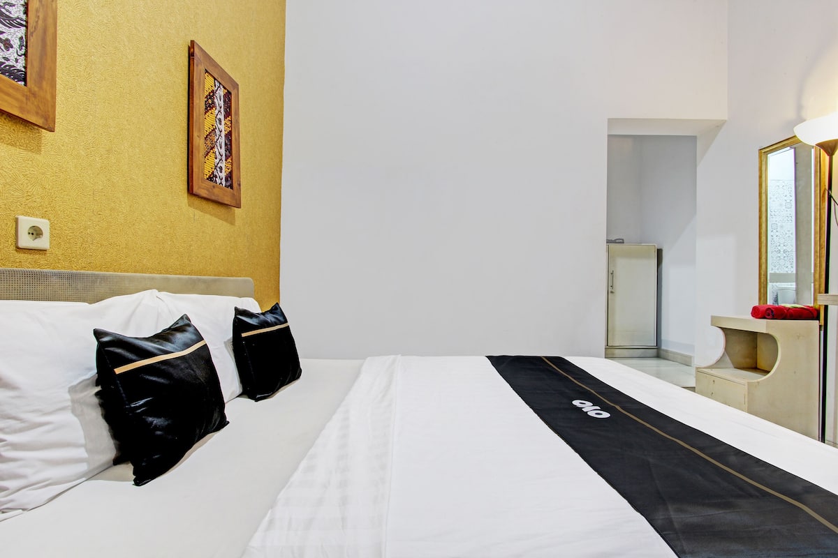 A hotel room with a bed, pillows, a headboard, a bedside table, a mirror, and a wall-mounted light fixture.
