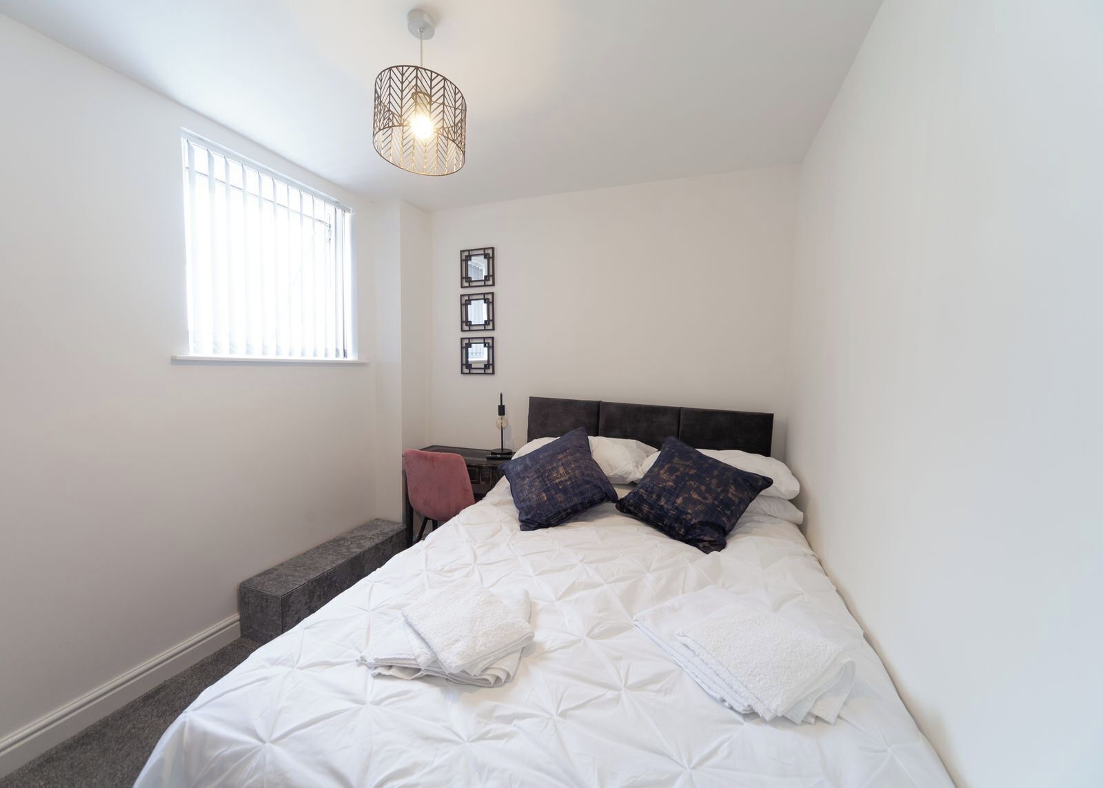 A bedroom with a bed, a desk, a chair, a window, and a hanging light fixture.