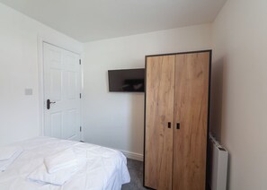 A bedroom with a bed, a wardrobe, and a television mounted on the wall.