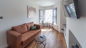 A living room with a brown sofa, a small round table, and a TV mounted on the wall. - Beautiful 7 bedroom Victorian home in Lancashire (Morecambe)