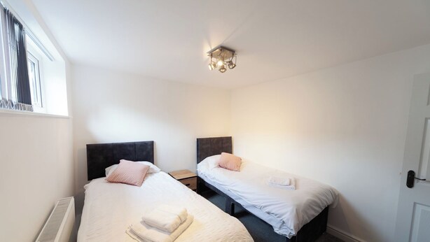A bedroom with two beds, a radiator, a window with curtains, and a ceiling light fixture. - Beautiful 7 bedroom Victorian home in Lancashire (Morecambe)