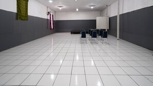 Ein Konferenzraum mit weißen Fliesen, einer Whiteboard-Tafel und mehreren in Reihen angeordneten Stühlen.