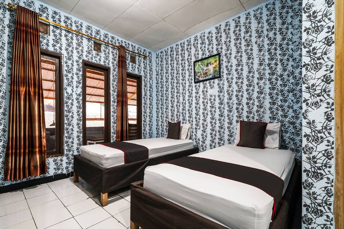 A room with two beds, a window, and a curtain rod.