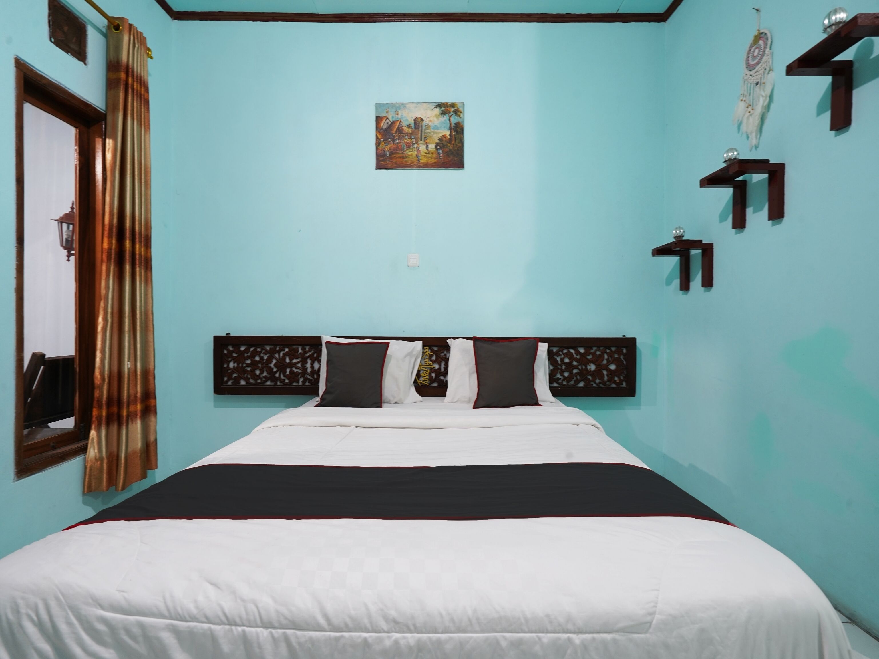 A bedroom with a bed, a painting, and a dreamcatcher.
