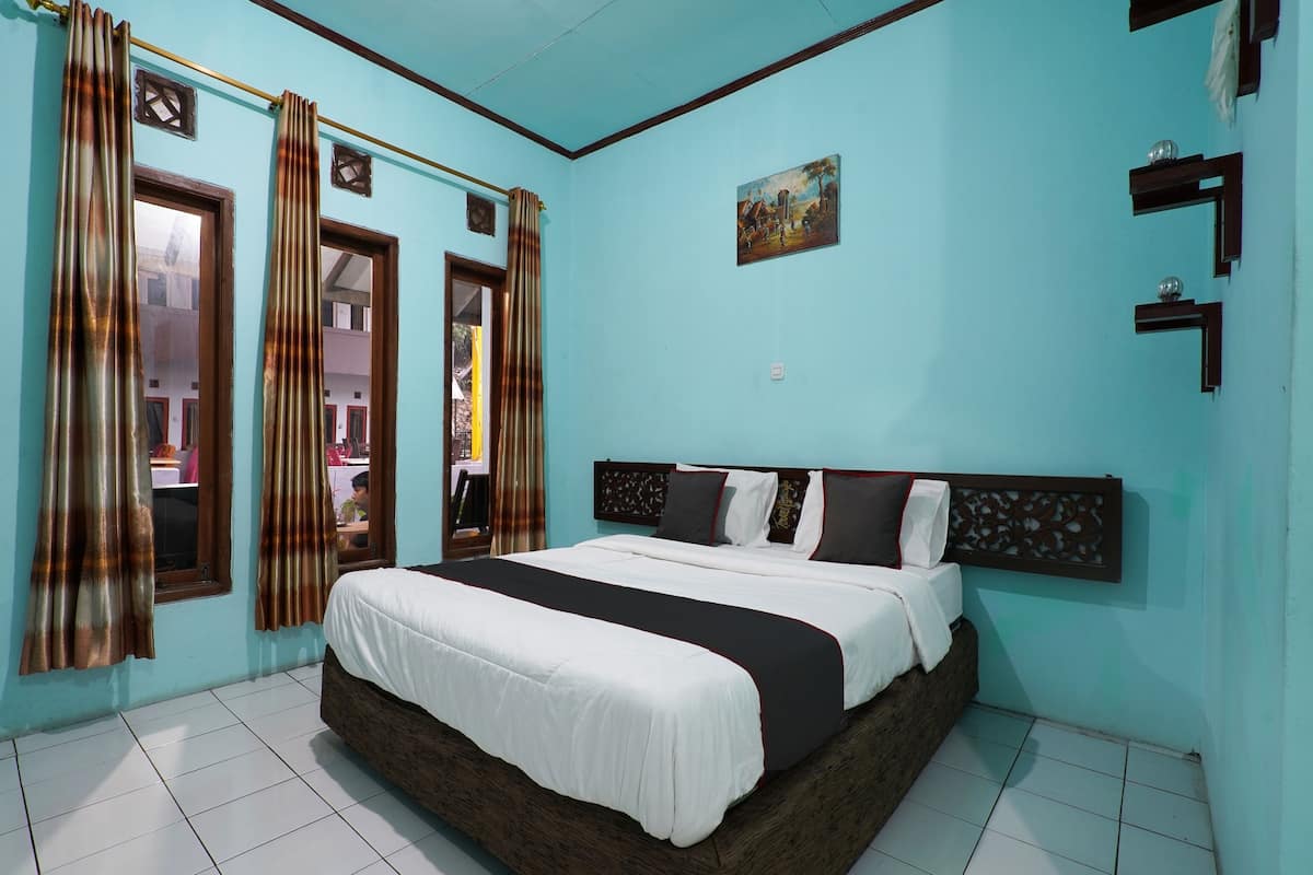 A bedroom with a large bed, curtains, a painting, and a tiled floor.