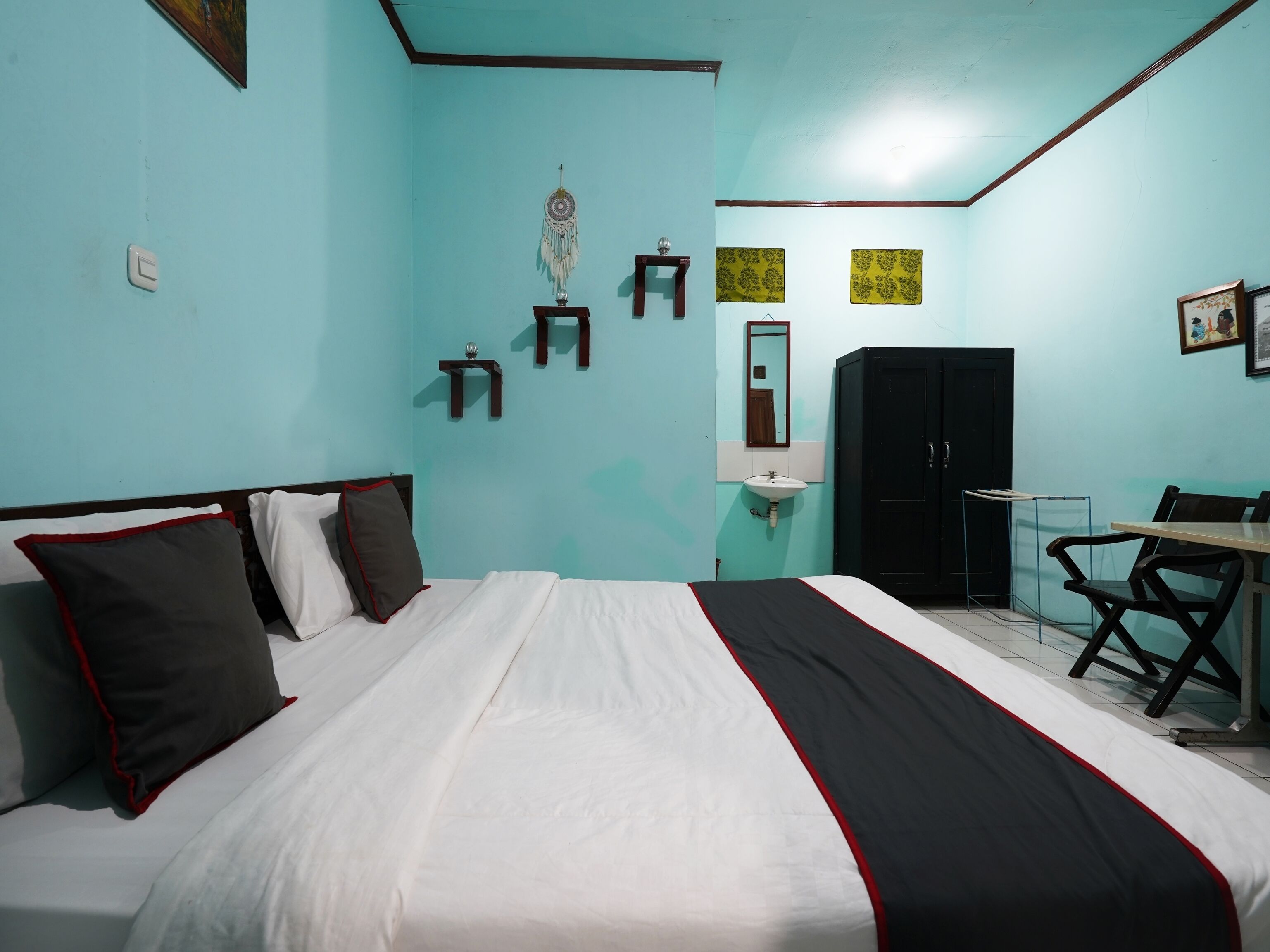 A bedroom with a bed, a desk, a chair, a wardrobe, a mirror, and a wall-mounted dreamcatcher.