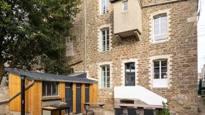 Ein Steinhaus mit einer Holz-Sitzterrasse und einem kleinen Holzbau mit Metall-Dach.