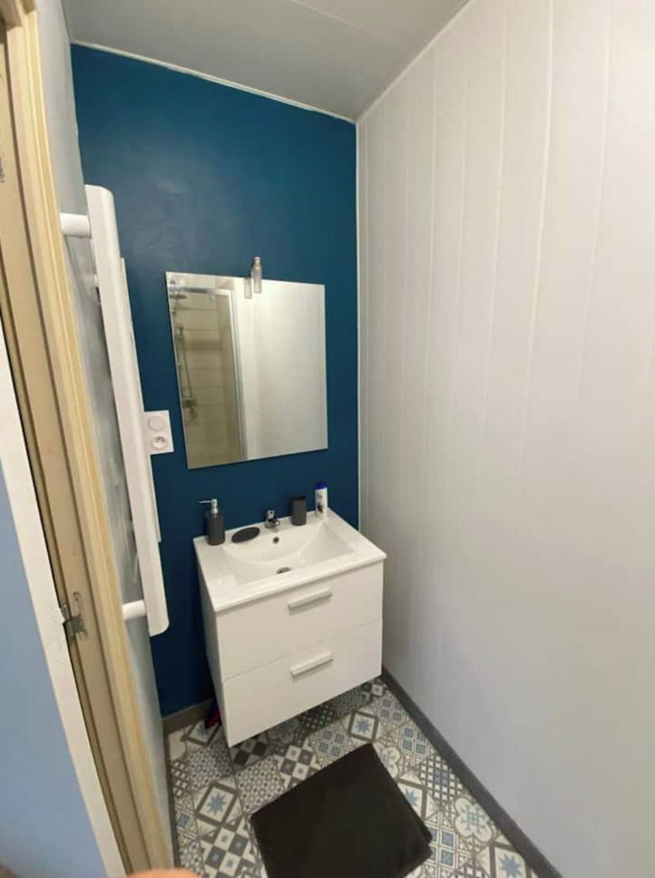 A bathroom with a white sink, a mirror, and a patterned floor.