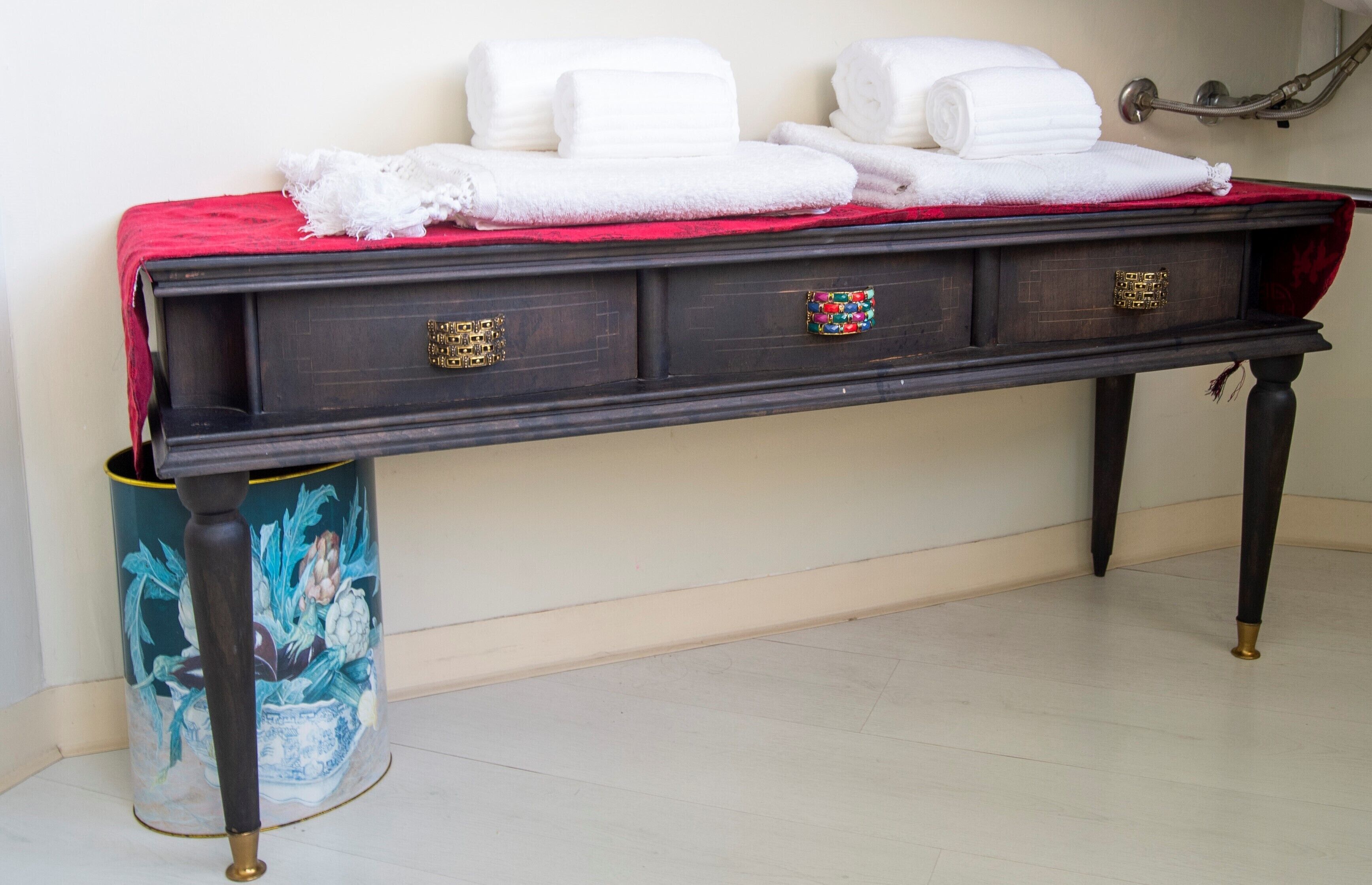 Un mobile da bagno in legno scuro con un panno rosso, asciugamani bianchi e un cestino decorativo.