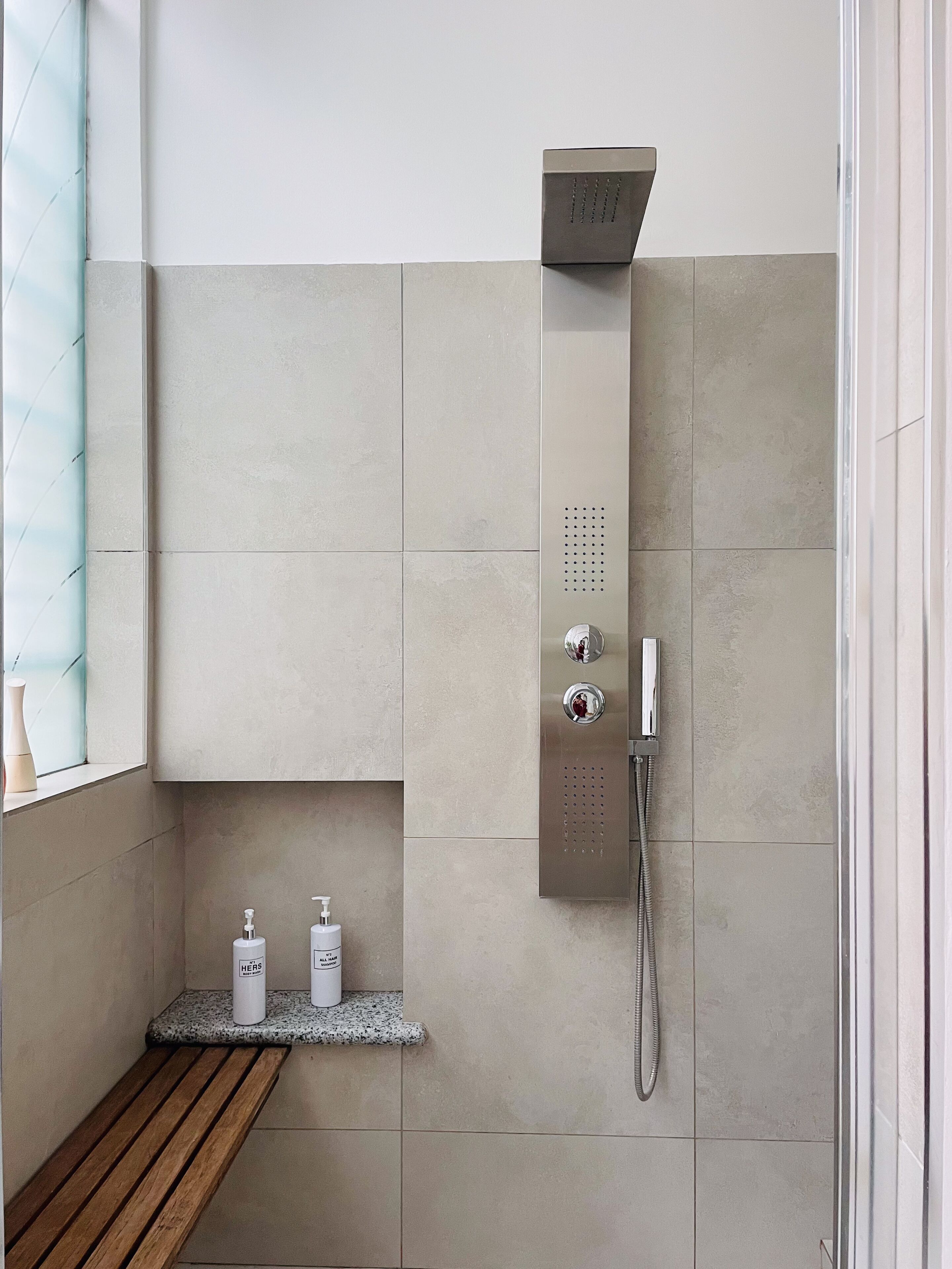 Une salle de bain moderne avec une douche, un banc et deux bouteilles de shampoing.