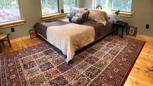 A bedroom with a large bed, multiple windows, a wooden floor, and a patterned rug. - The Glacier Nook (Deming)