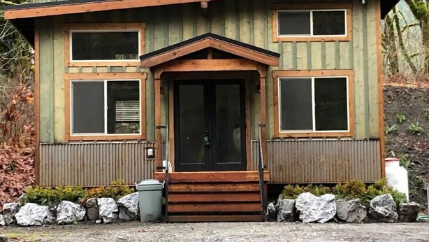 A small, two-story wooden cabin with a central entrance, large windows, and a stone foundation. - The Glacier Nook (Deming)