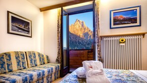 A hotel room with a sofa, a bed with a floral bedspread, a towel, a framed picture of a mountain, and a radiator.