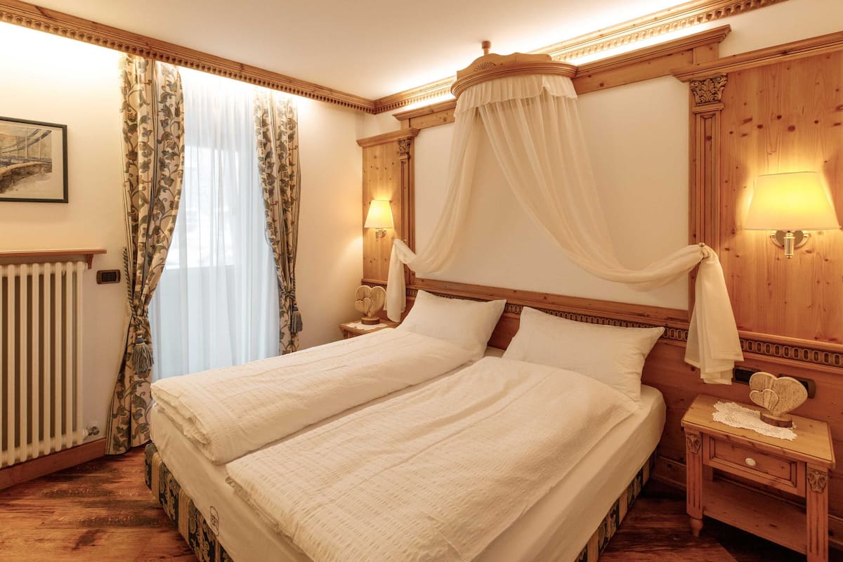 Una cama doble con dosel, dos mesitas de noche con lámparas, un radiador y suelo de madera.