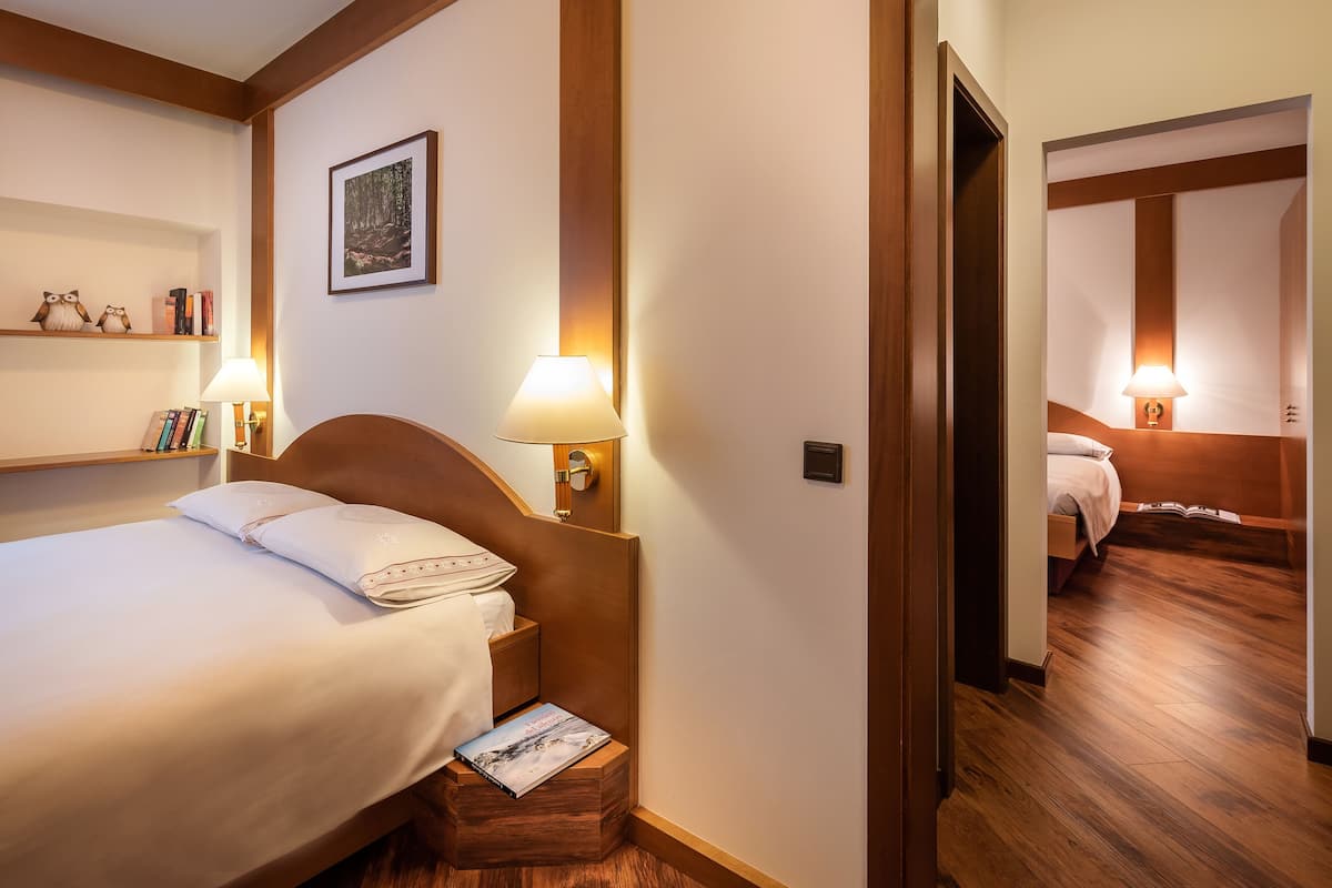 Habitación de hotel con una cama bien hecha, una lámpara de noche, una mesita de noche con un libro, un cuadro en la pared y piso de madera.
