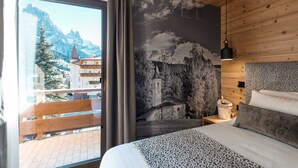 A bedroom with a large window, a mural of mountains, a wooden ceiling, and a bed with patterned bedding.