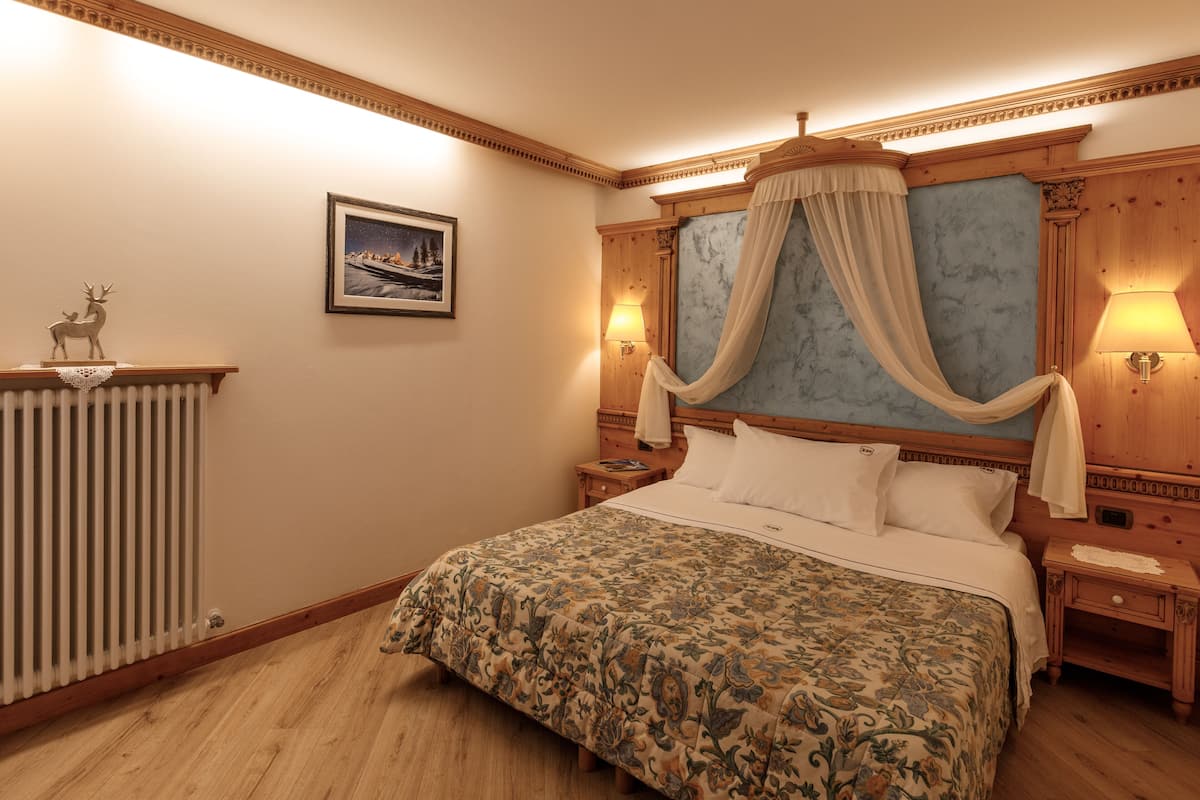 Un dormitorio con una cama grande, una mesita de noche, un cabecero de madera, un cuadro en la pared y un radiador.