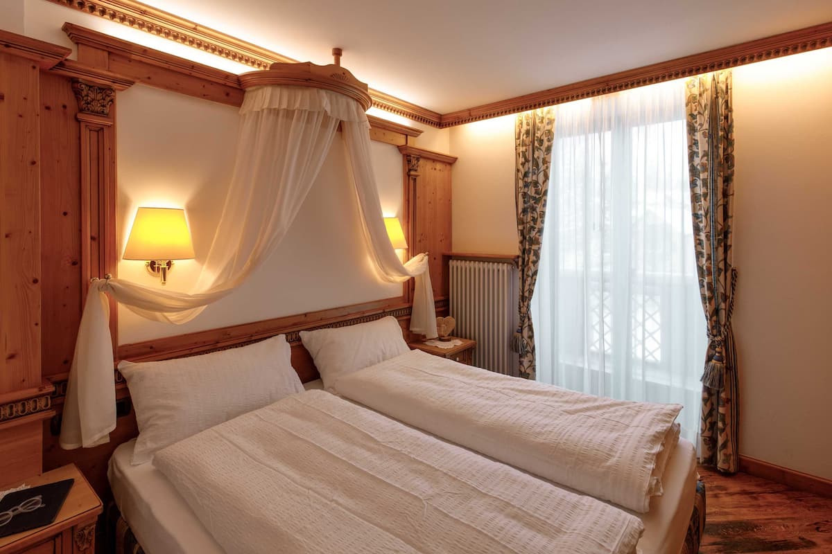 Una cama doble con dosel, dos lámparas de noche, un cabecero de madera y una ventana con cortinas.