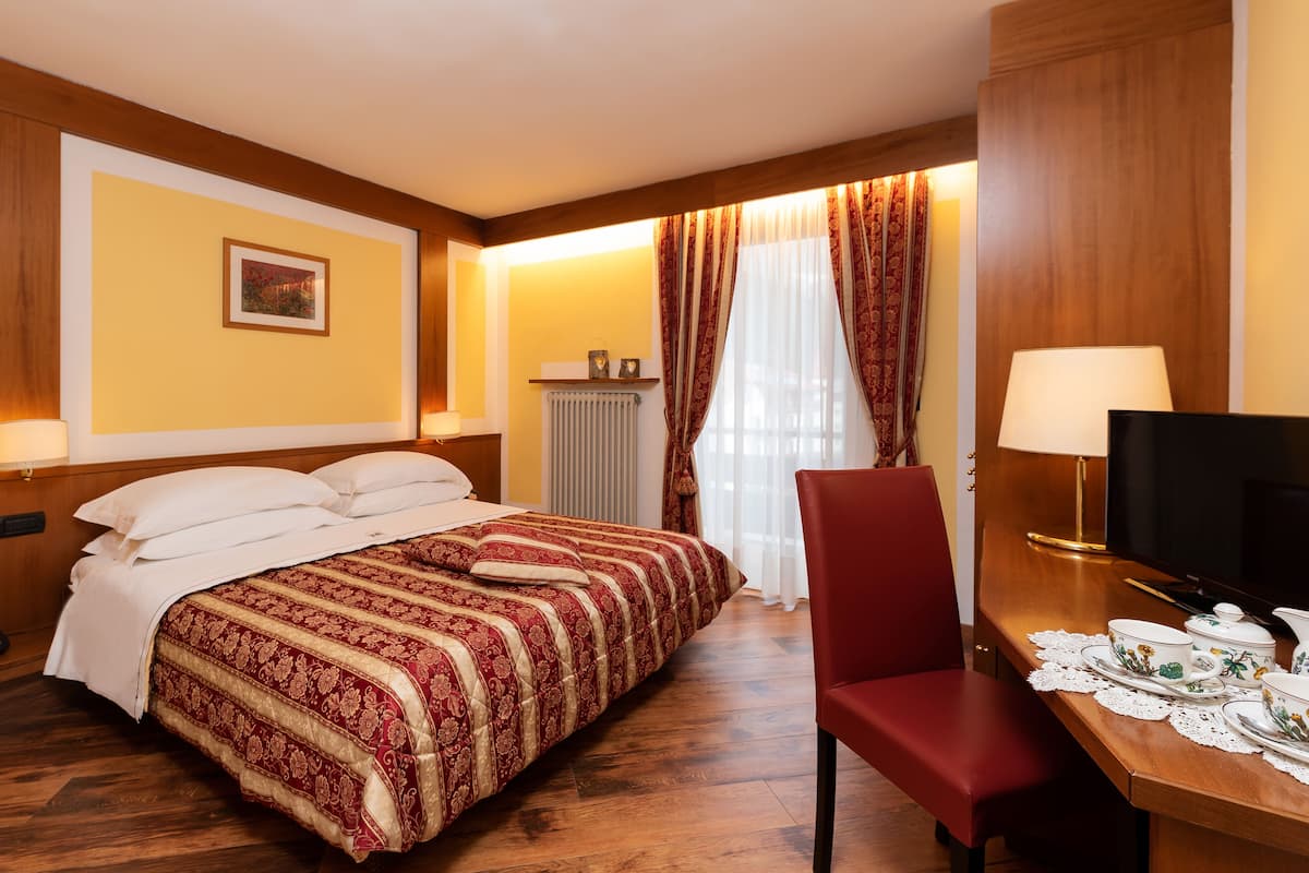 Habitación de hotel con una cama grande, un escritorio de madera con silla, un televisor y un radiador.