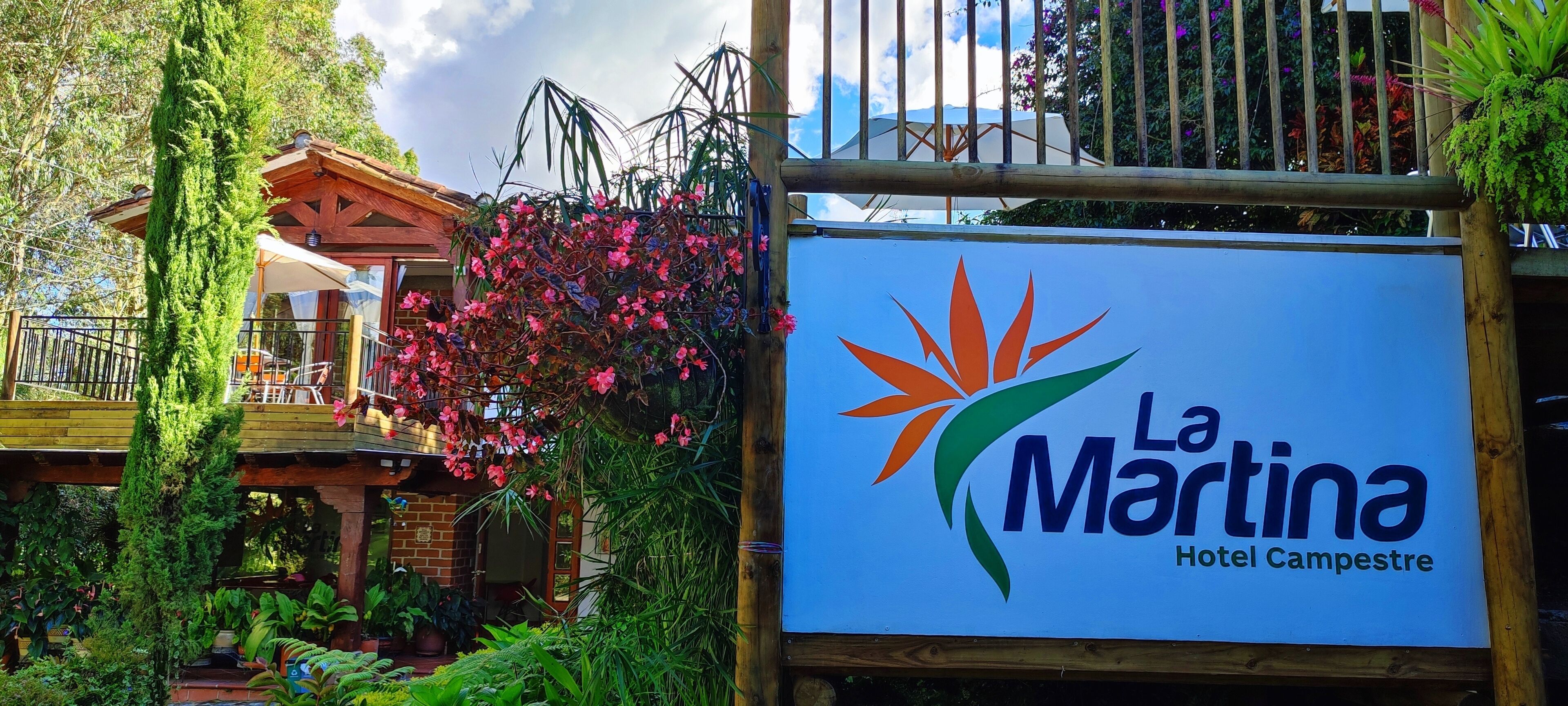 Een bord voor Hotel La Martina Campestre met een logo met een gestileerde zon en groene bladeren.