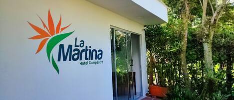 Exterior del Hotel La Martina Campestre, con un logo que presenta un sol estilizado y hojas verdes.