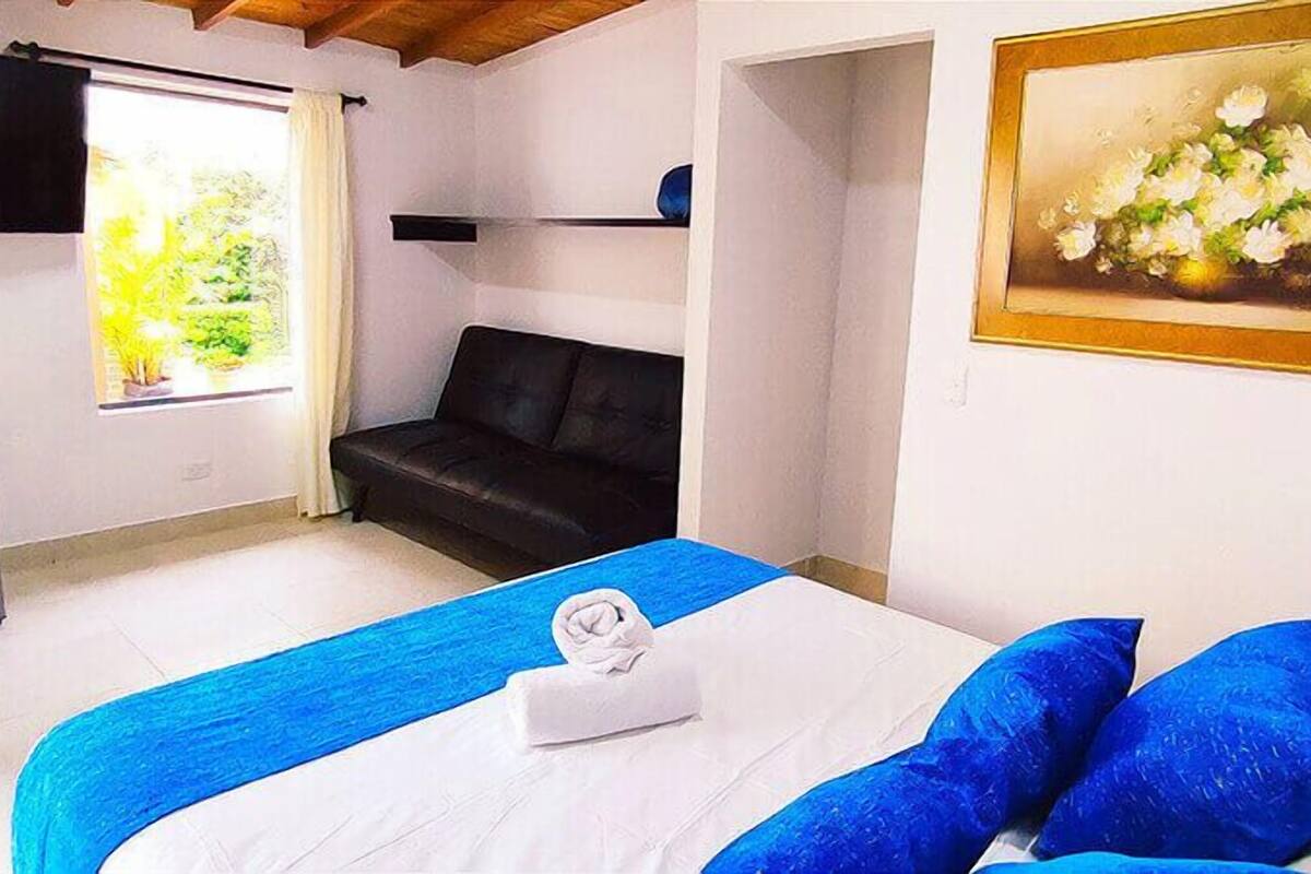 Un dormitorio con cama, sofá, un cuadro, lámpara y ventana con cortinas.