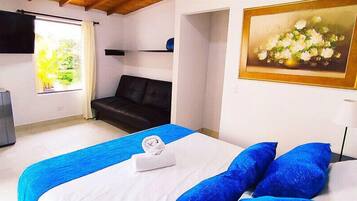 A bedroom with a bed, a sofa, a painting, a lamp, and a window with curtains.