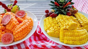 Two plates of fruit on a checkered tablecloth.