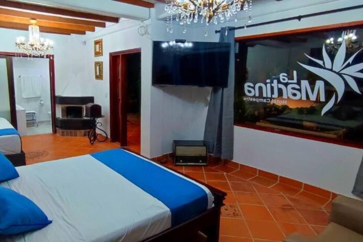 Habitación de hotel con tres camas, televisor, candelabro y un ventanal grande con un logotipo.