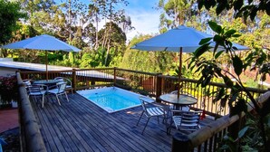 A wooden deck with a hot tub, two umbrellas, and outdoor seating.