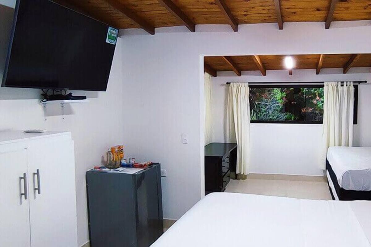 Una habitación con cama, televisión, escritorio y ventana con cortinas.