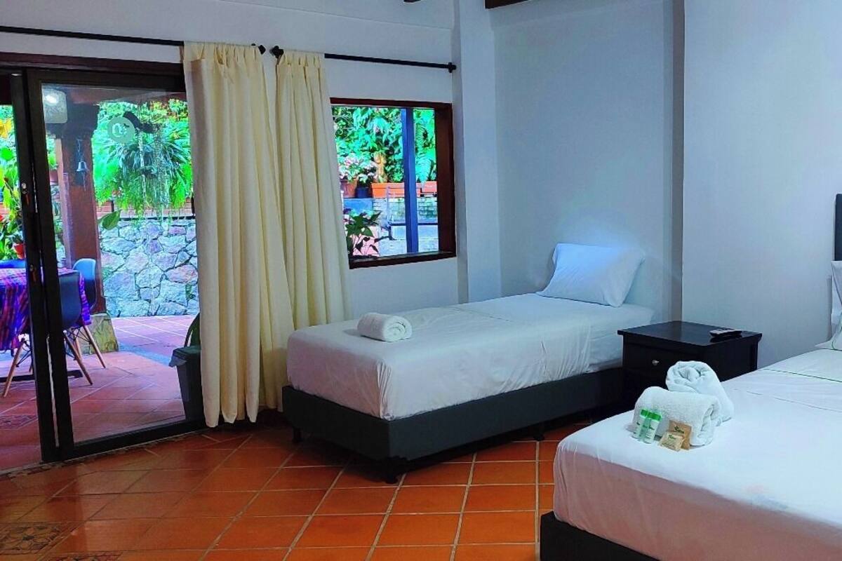 Habitación de hotel con dos camas, una puerta corrediza de vidrio que da a un área exterior y una mesita con artículos de aseo.